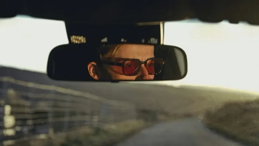 Homme portant des lunettes de soleil rouges, vu dans un rétroviseur de voiture, symbolisant le confort visuel et le style en conduite chez Regards Uniques