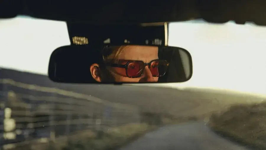 Homme portant des lunettes de soleil rouges, vu dans un rétroviseur de voiture, symbolisant le confort visuel et le style en conduite chez Regards Uniques